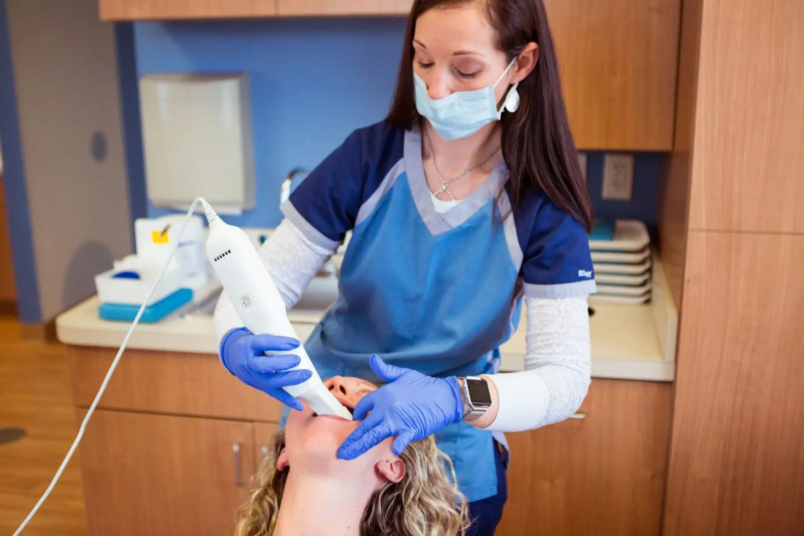 A woman in blue scrubs is getting her teeth checked.