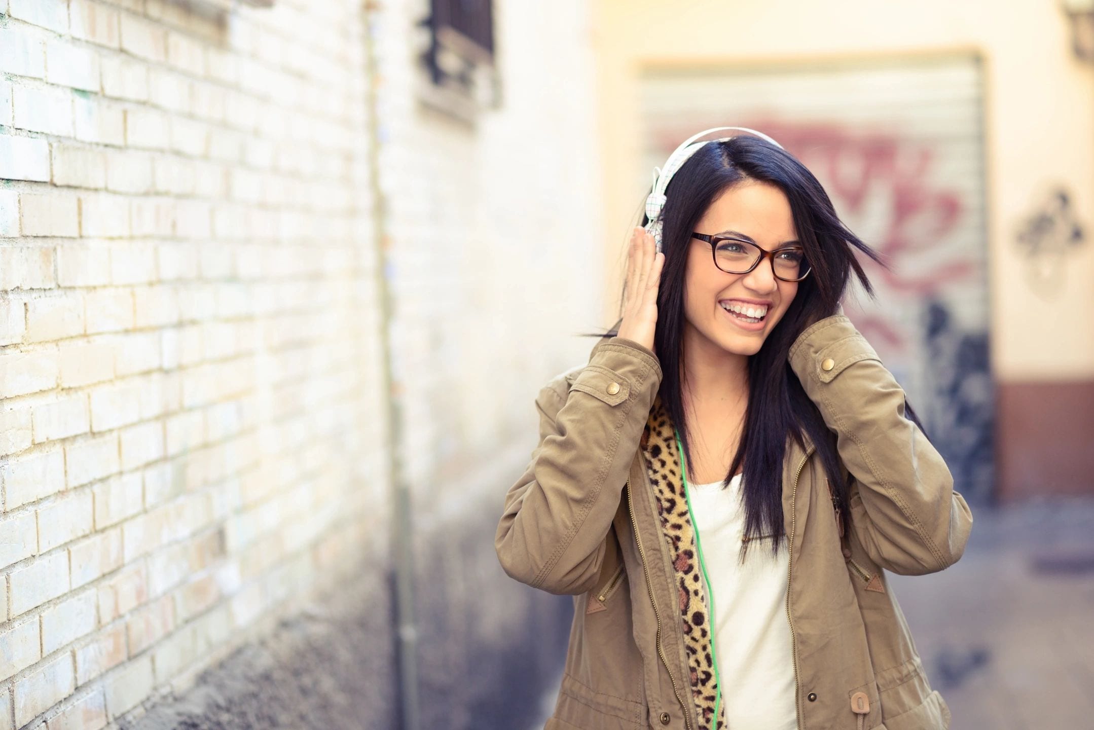 A woman with glasses and headphones is smiling.